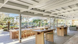Un espace de restauration en plein air avec des tables et des chaises en bois, une grande table centrale et une vue sur le jardin environnant.