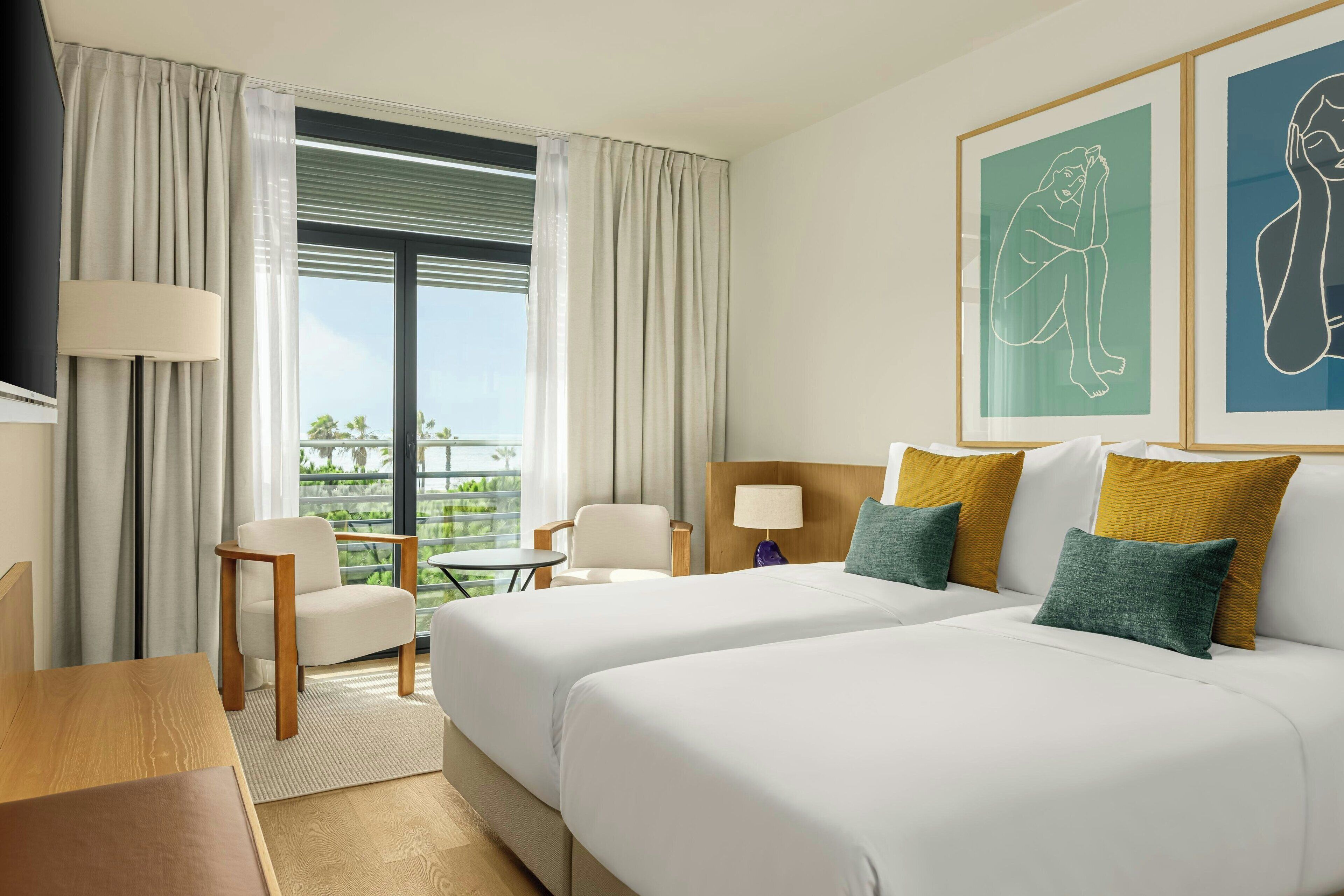 Ein Hotelzimmer mit zwei Betten, einem Schreibtisch, einem Stuhl und Blick ins Freie.