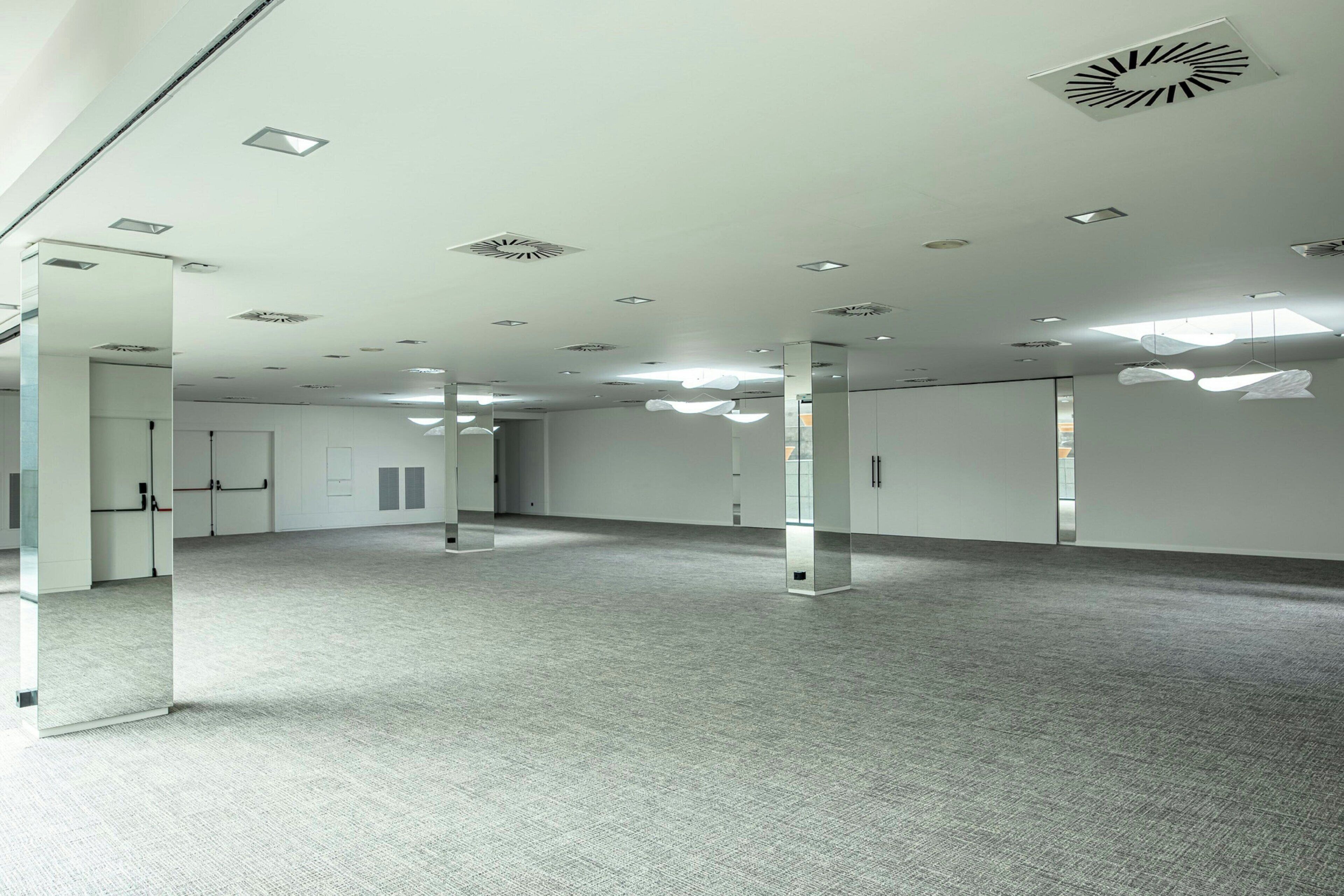 Una habitación amplia y moderna con techo alto, iluminación empotrada y piso alfombrado.