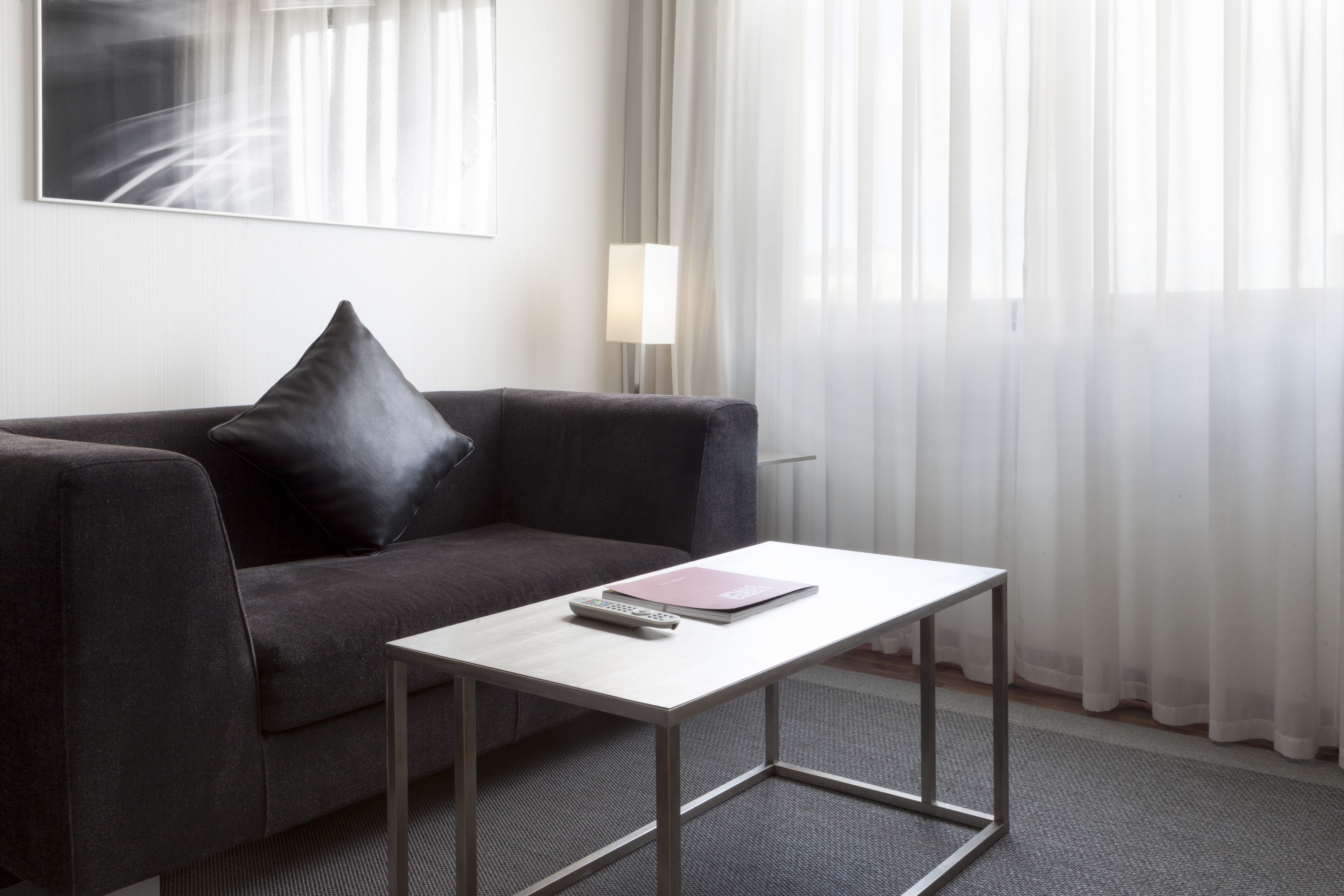 A modern room with a grey sofa, a small white table, a remote control, and a pink notebook.