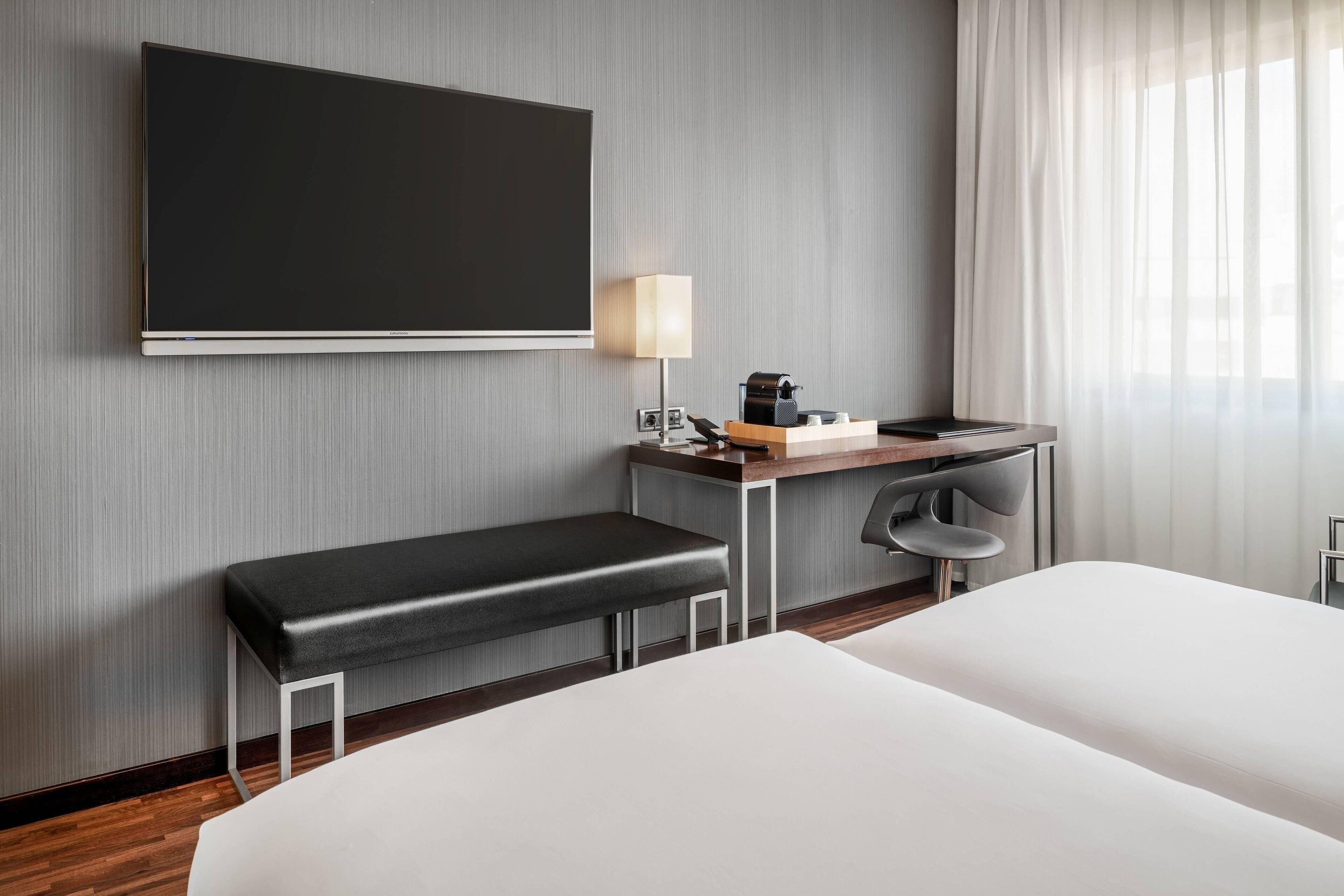 A hotel room with a large bed, a desk with a lamp, a coffee maker, and a TV mounted on the wall.