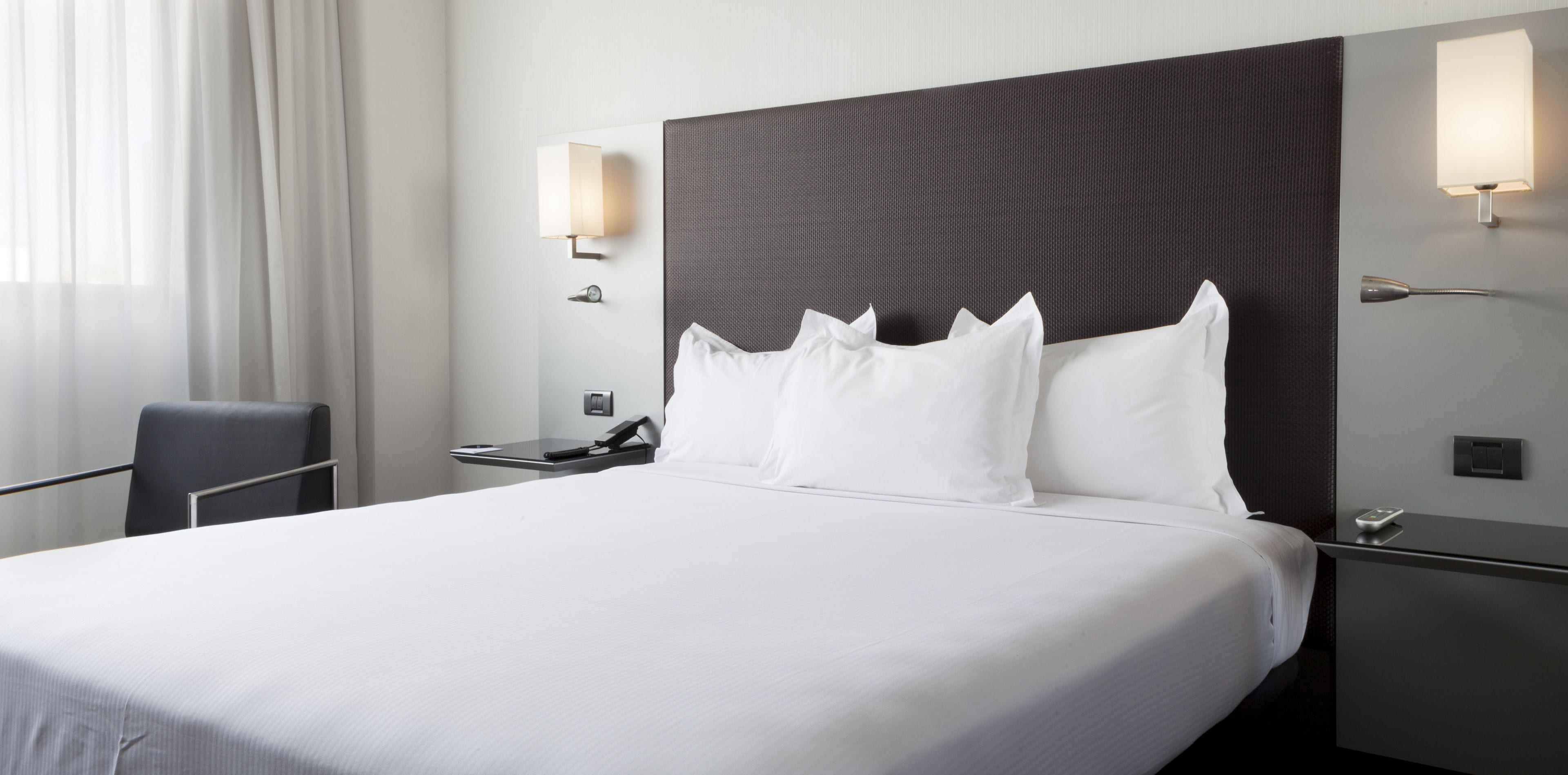A hotel room with a large bed, two bedside tables, a chair, and two wall-mounted lamps.