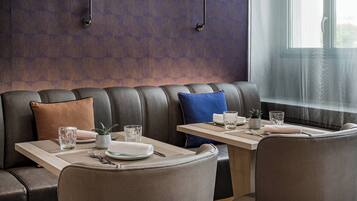 A modern dining area with a leather booth seating, a wooden table with a placemat, and a window with sheer curtains.