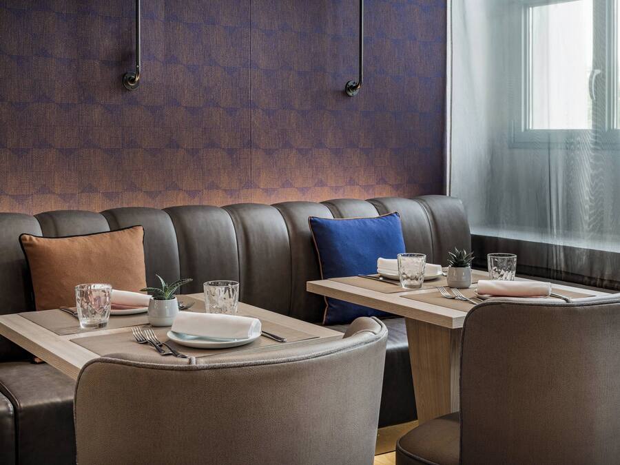 A modern dining area with a leather booth seating, a wooden table with a placemat, and a window with sheer curtains.