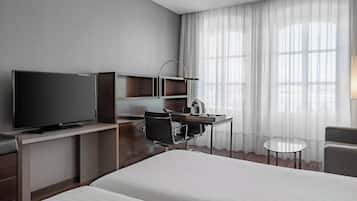 A hotel room with a bed, a desk with a chair, a television, a small table, and a window with curtains.