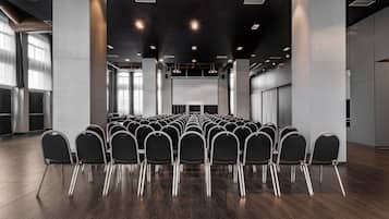 A conference room with rows of chairs facing a large screen, wooden flooring, and modern lighting fixtures.