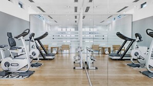 Een sportschool met spiegelwanden, fitnessapparatuur en een houten vloer.