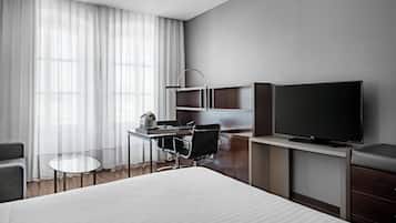 A modern hotel room with a large bed, a desk with a chair, a flat-screen TV, a coffee machine, and a small table.
