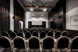 Un salón de conferencias con filas de sillas, una pantalla de proyector y una pizarra.