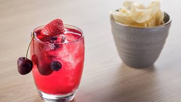 Un vaso de bebida roja con fresas y arándanos, y un cuenco de papas fritas.