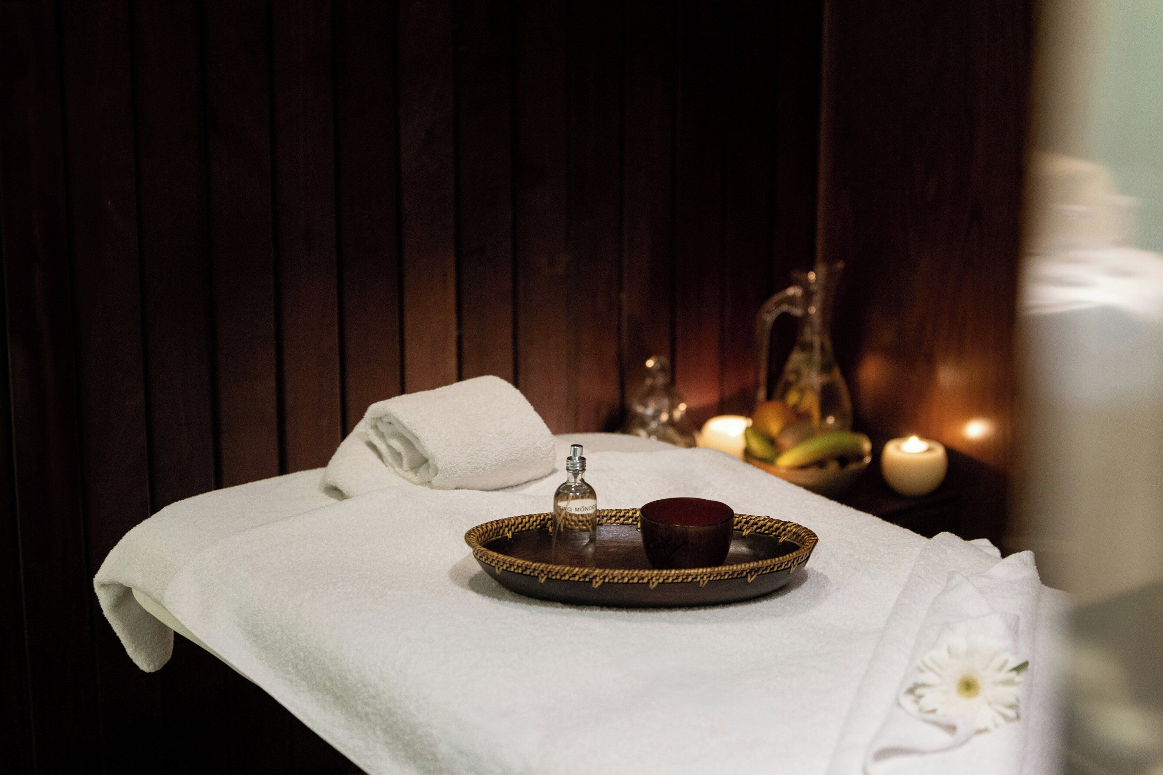 Een wellness omgeving met een handdoek, een dienblad met een fles en een beker, kaarsen en een decoratief glas.