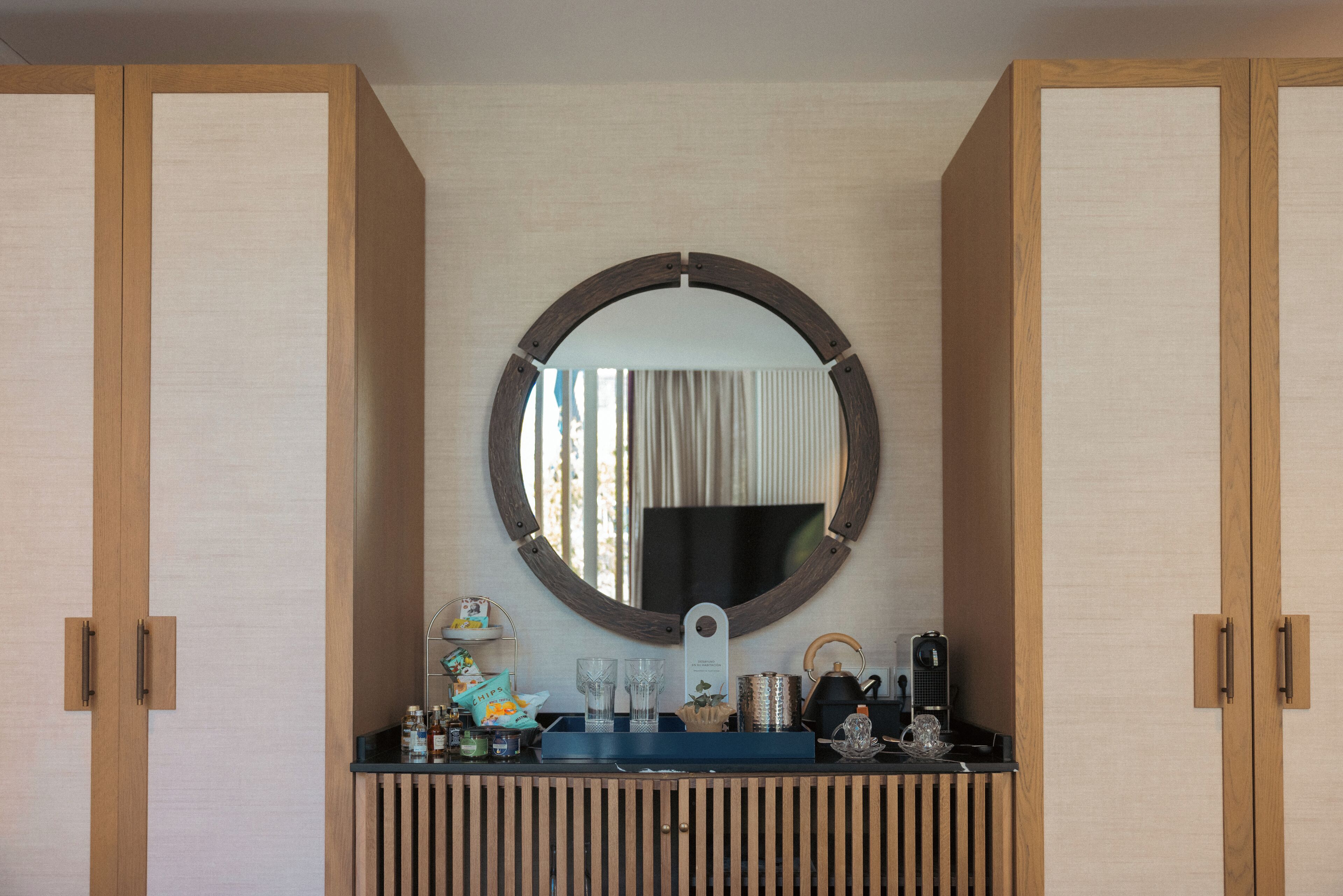 A bathroom with wooden cabinets, a round mirror, and a vanity with toiletries.