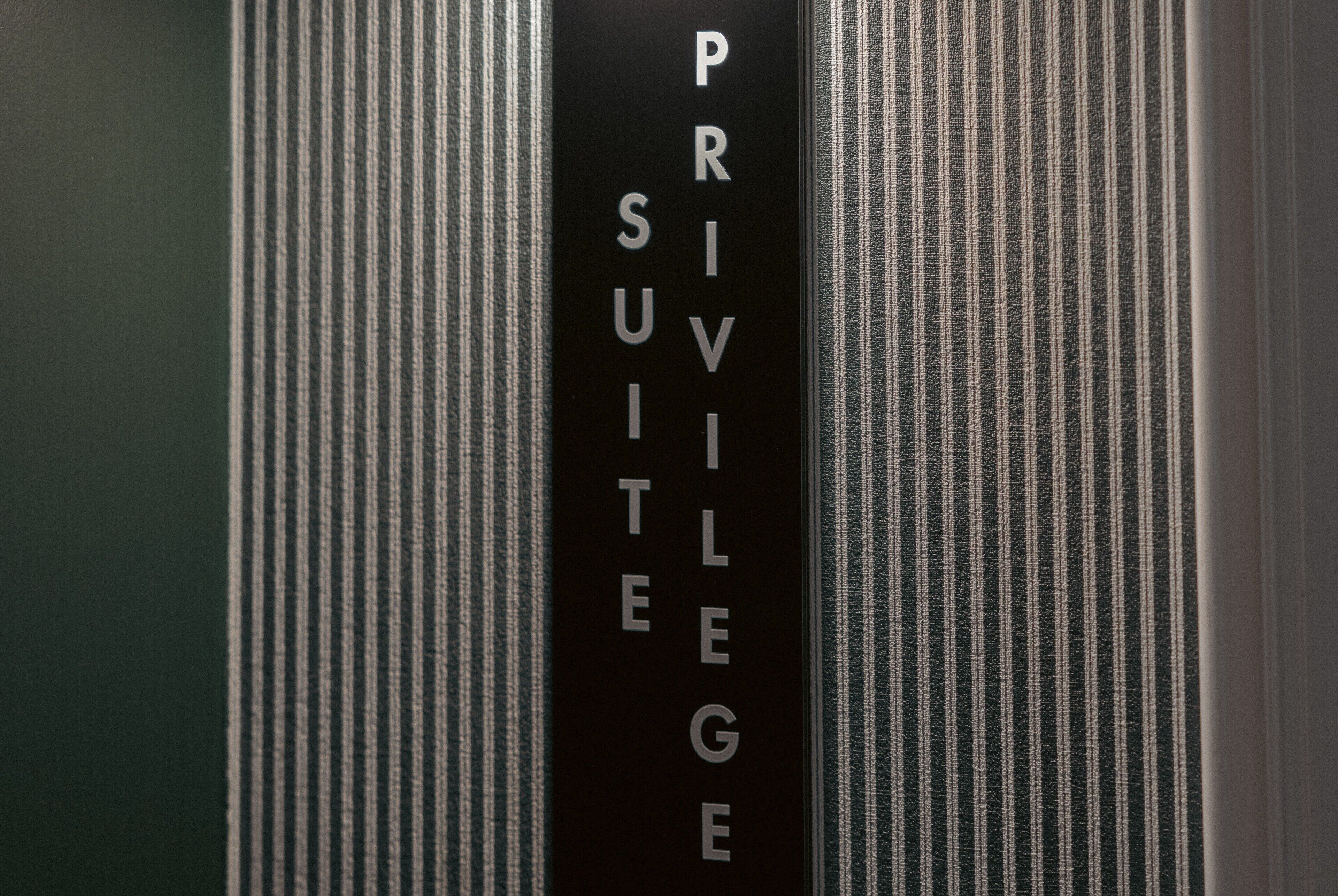 Een zwart bord met de tekst 'PRIVILEGE SUITE' op een structuurwand.