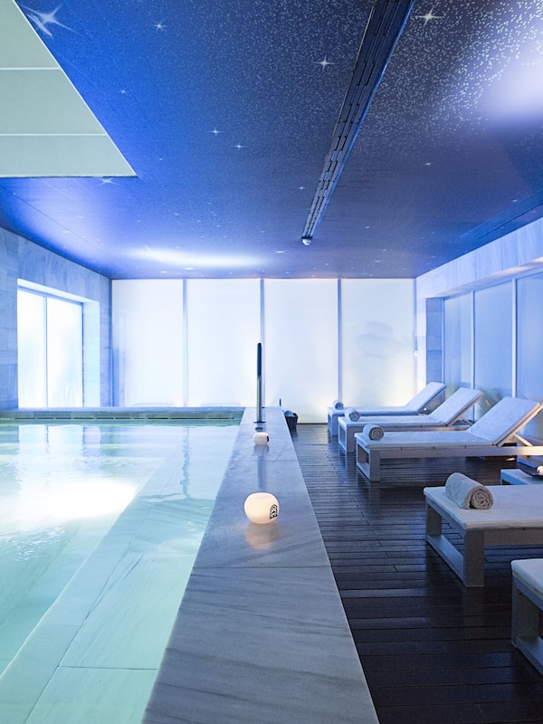 Relax in a serene spa room with a long pool, starry ceiling, and comfortable lounge chairs.