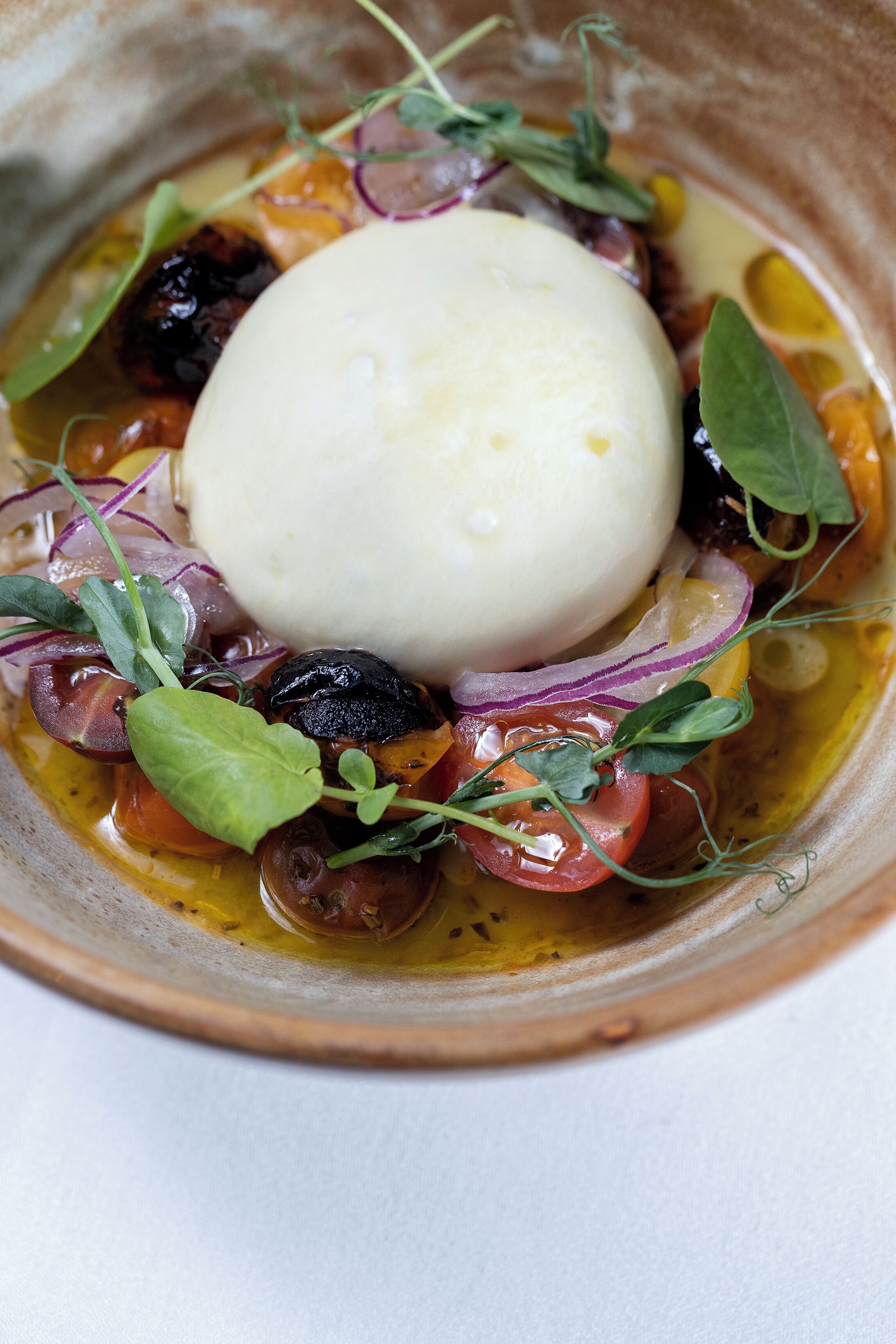 A dish with a poached egg, vegetables, and a creamy sauce in a ceramic bowl.