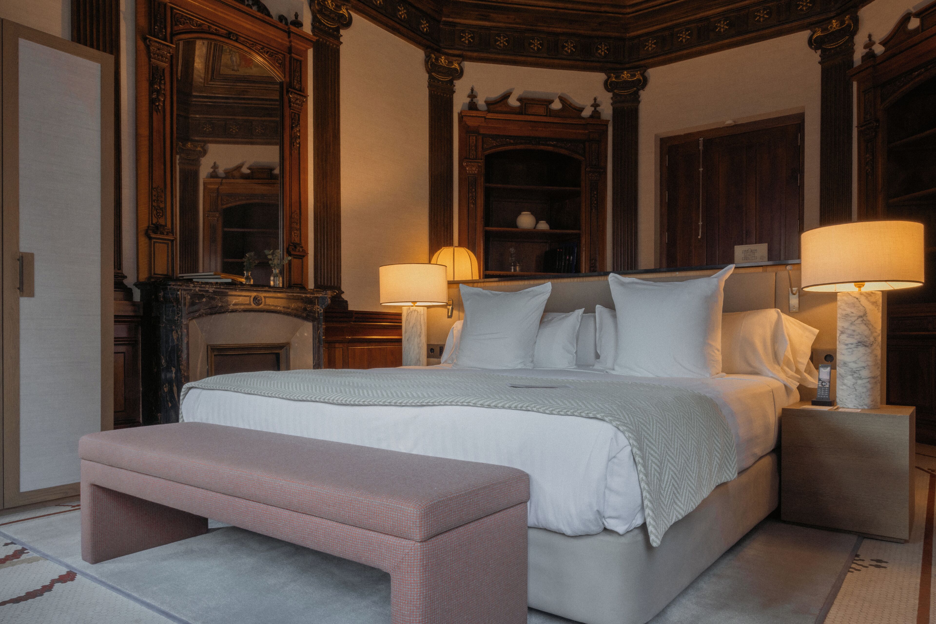 Un dormitorio con una cama grande, dos mesitas de noche, un banco, una chimenea y muebles de madera ornamentados.