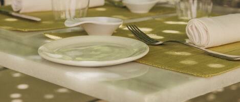 Una mesa de comedor con mantel blanco, individuales verdes y cristalería transparente.