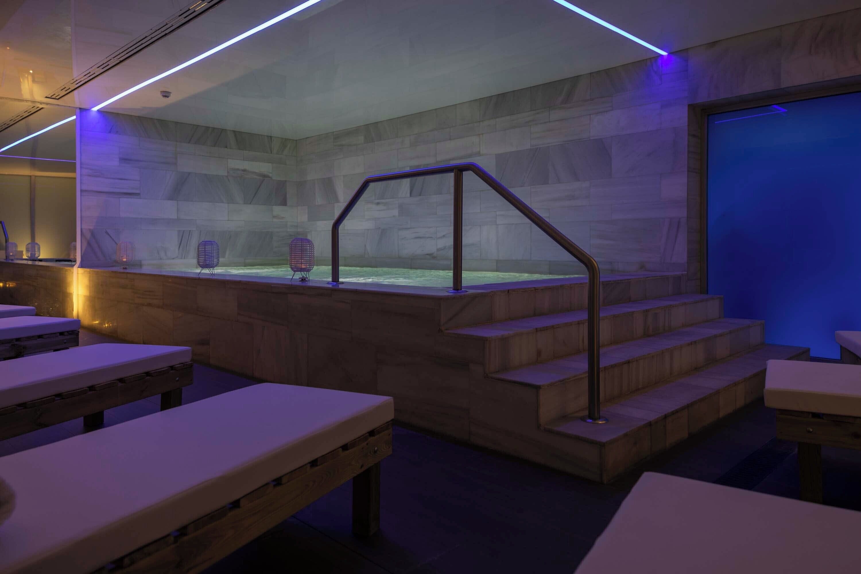 A modern spa area with wooden benches, a glass-enclosed hot tub, and a staircase with metal railings.