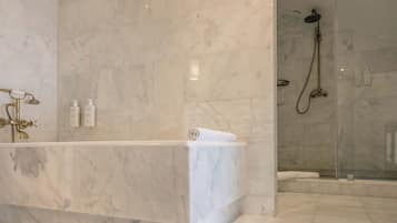 Un baño con lavamanos de mármol, ducha y cabina de ducha con paredes de vidrio.