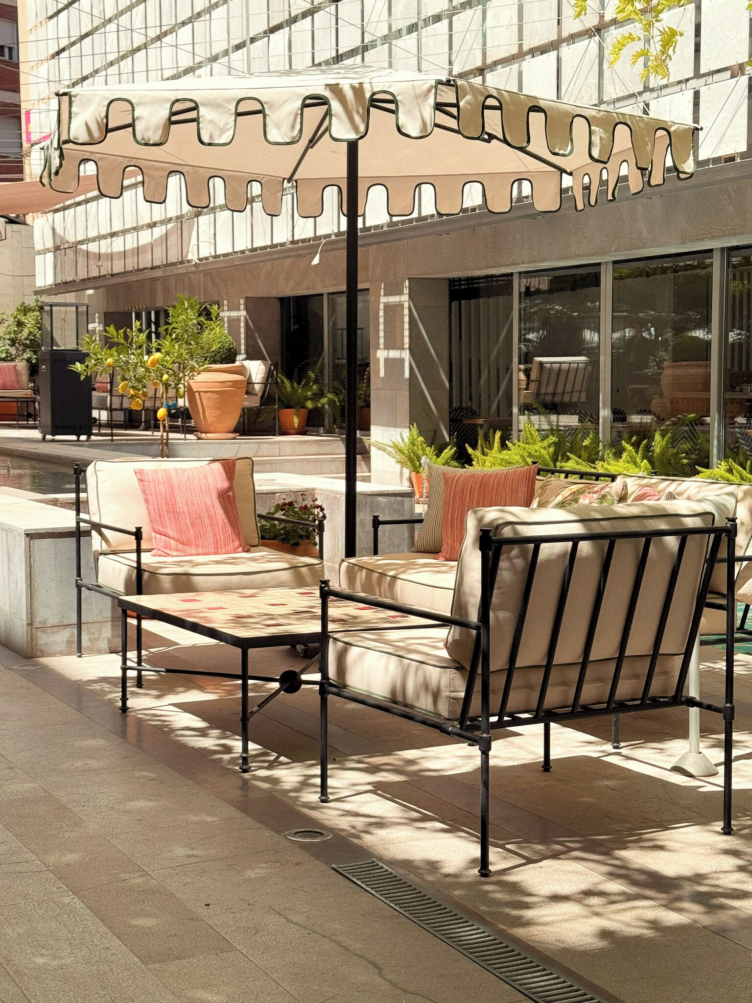 An outdoor seating area with cushioned chairs and a table, a large umbrella, and potted plants.