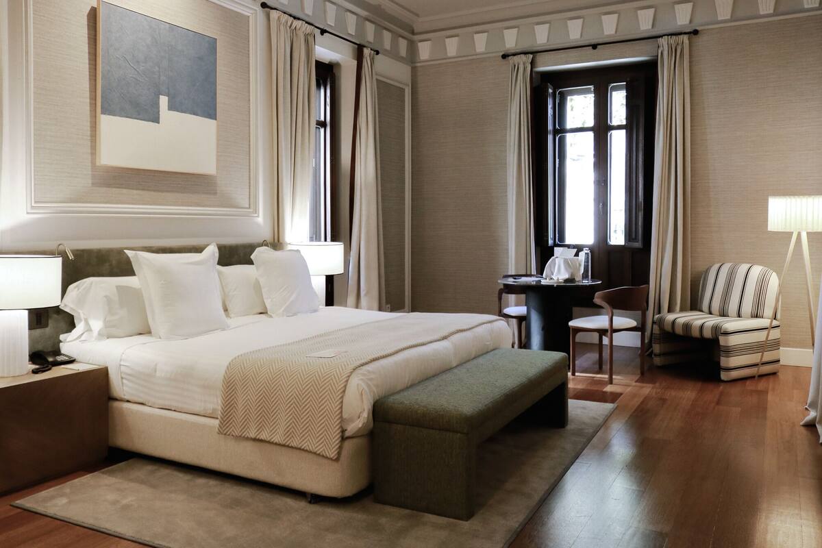 Ein Hotelzimmer mit einem großen Bett, Nachttischen, einem Schreibtisch mit Stuhl, einer Couch und einer Lampe.