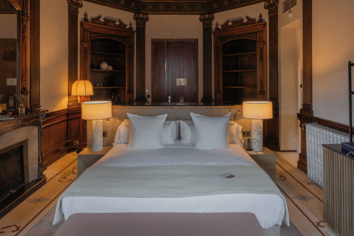 Ein geräumiges, stilvoll eingerichtetes Schlafzimmer mit einem großen Bett, zwei Nachttischlampen, einem Kamin und einem großen Spiegel über dem Bett.