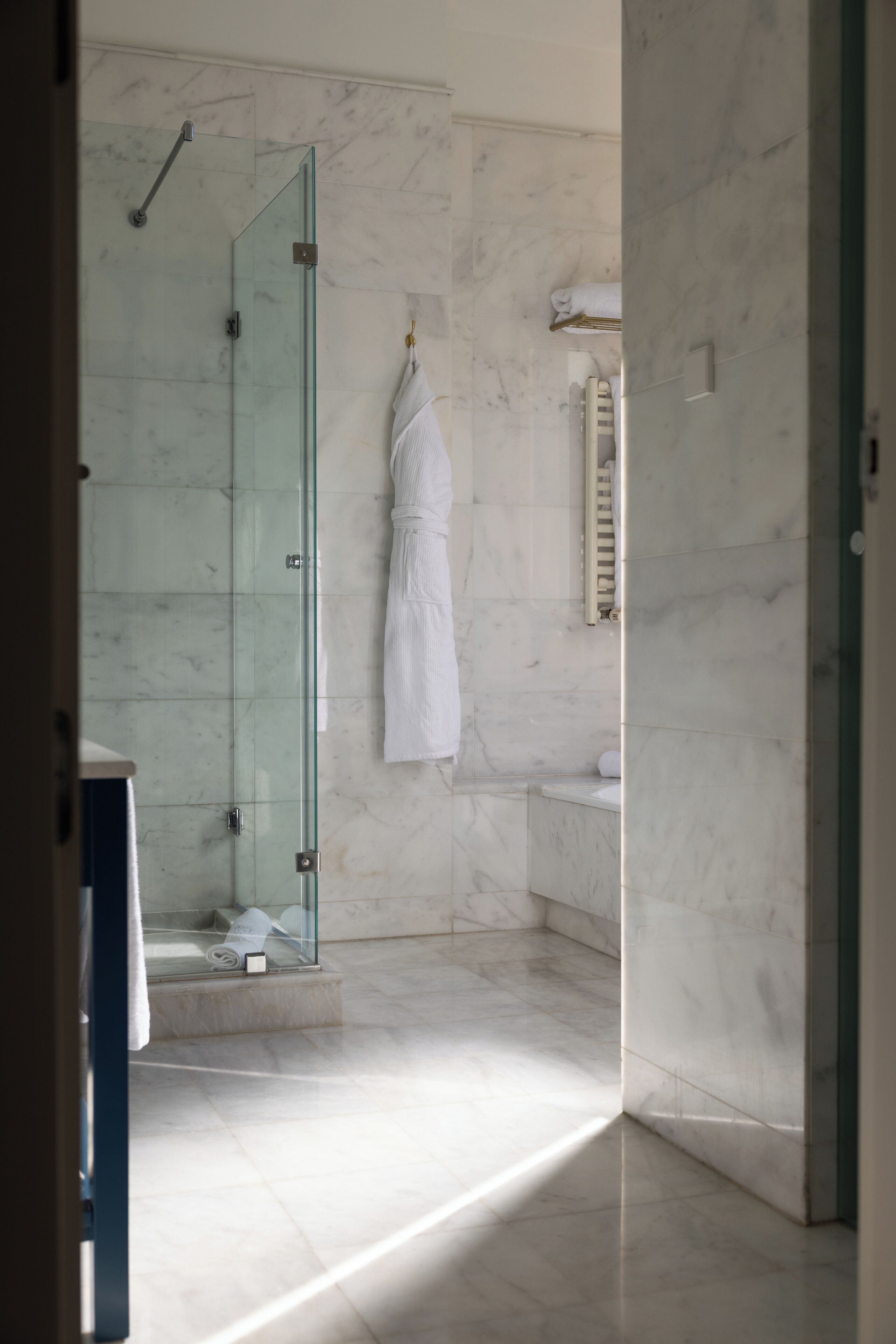 A modern bathroom with a glass shower enclosure, a white towel hanging on the wall, and a marble floor.