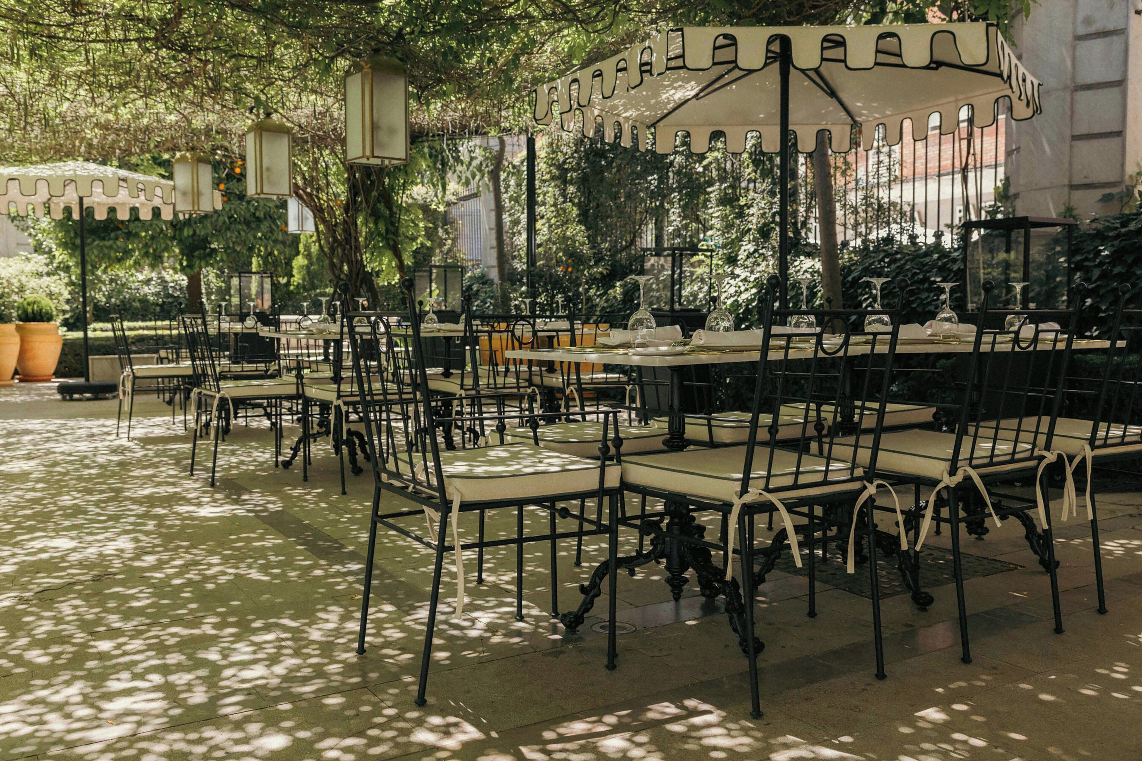 Tables et chaises pour les repas en plein air, entourées d’arbres, avec un bâtiment visible en arrière-plan.
