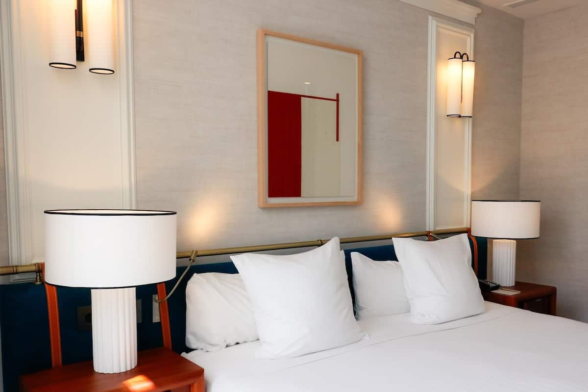 Ein Hotelzimmer mit einem Bett, zwei Nachttischlampen, einem gerahmten Kunstwerk an der Wand und einem Nachttisch mit Lampe.