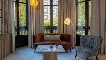 A modern living room with a brown sofa, a patterned armchair, a white coffee table, and large windows with curtains.