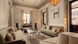 A spacious living room with a sofa, armchair, and coffee table, large windows with curtains, and a chandelier. - Hospes Palacio de los Patos, a Member of Design Hotels (Granada)