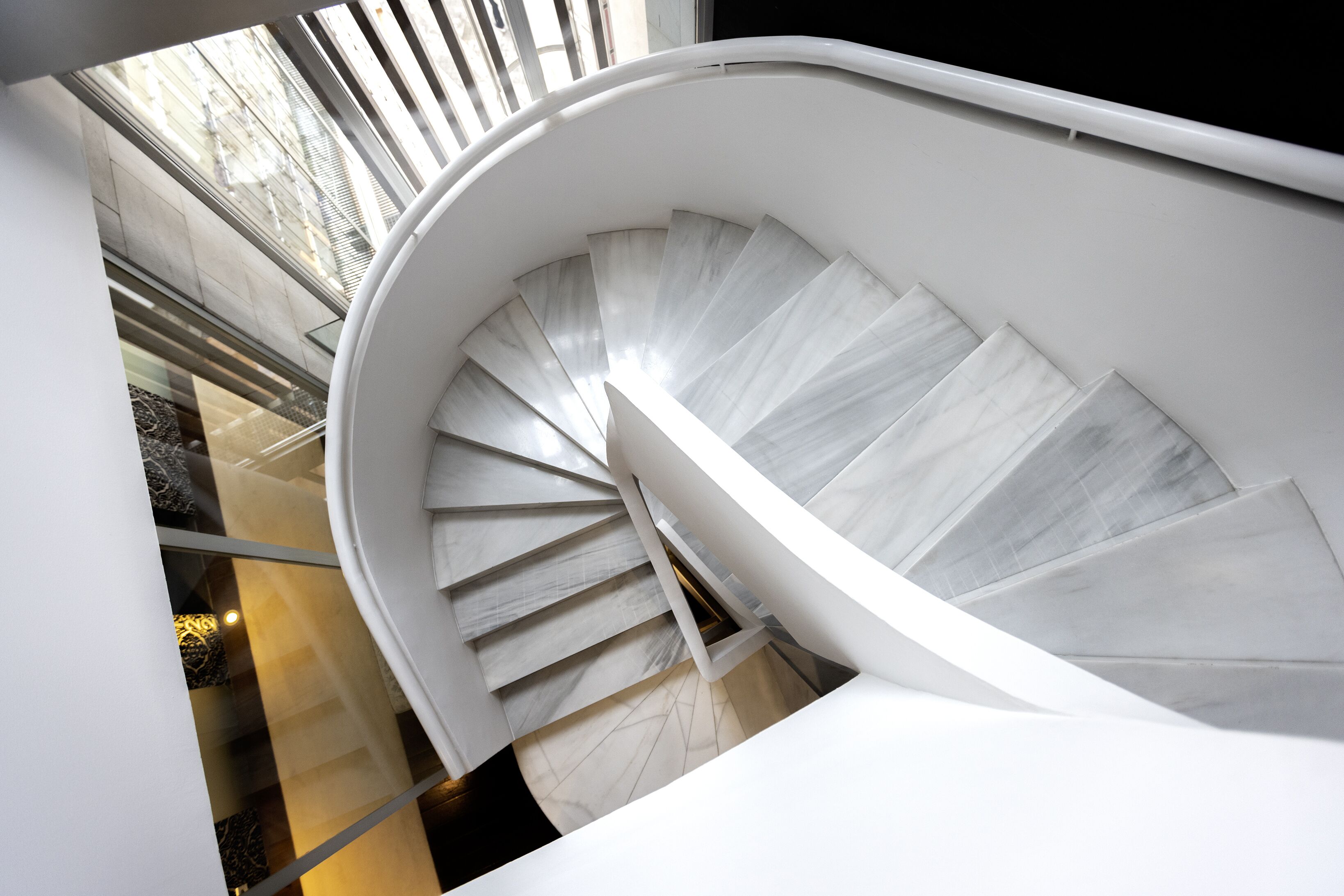 A spiral staircase with a white railing and marble steps, leading to an upper floor.