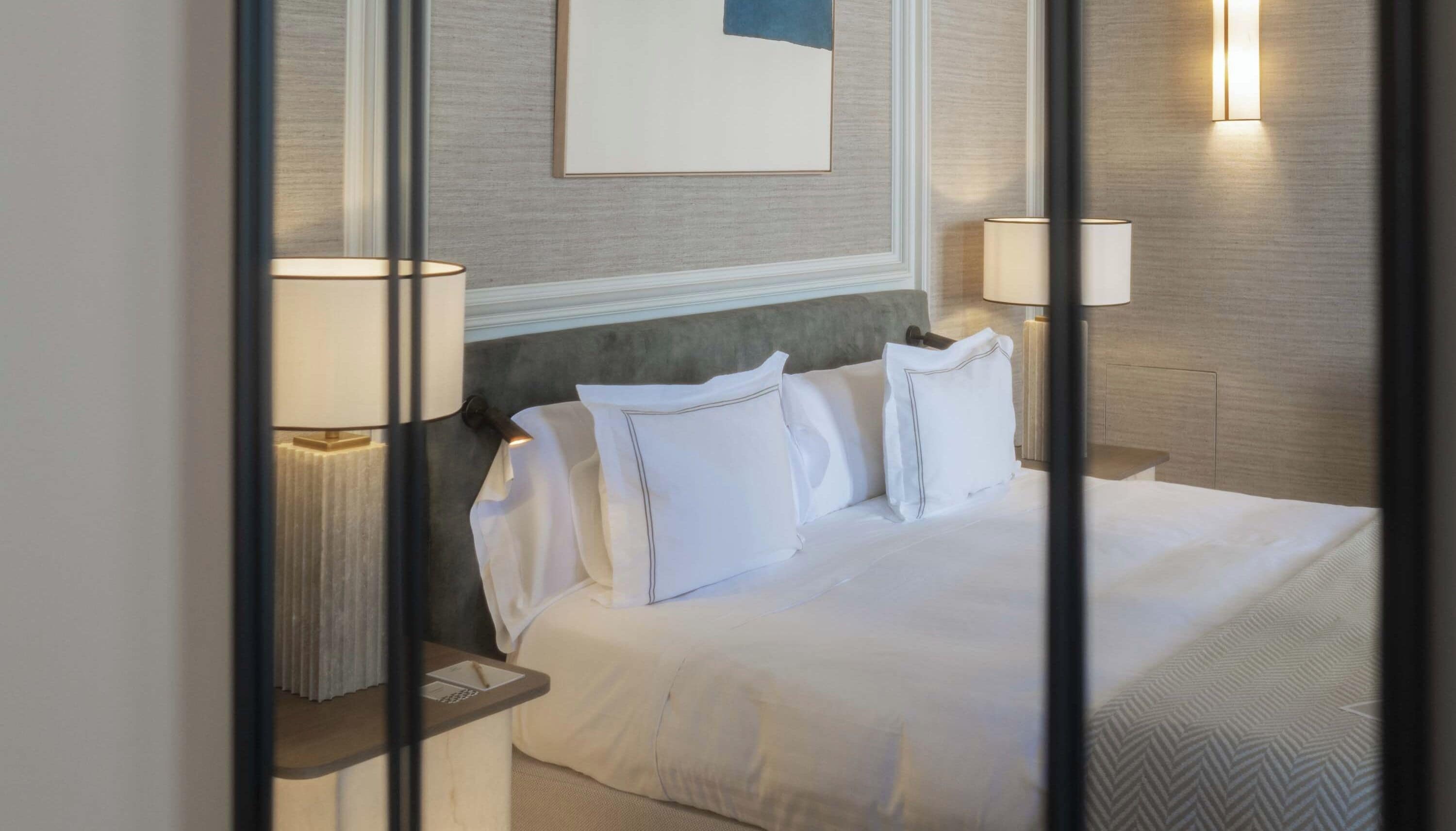 A neatly made bed with white linens and pillows, two bedside lamps, and a framed picture on the wall.