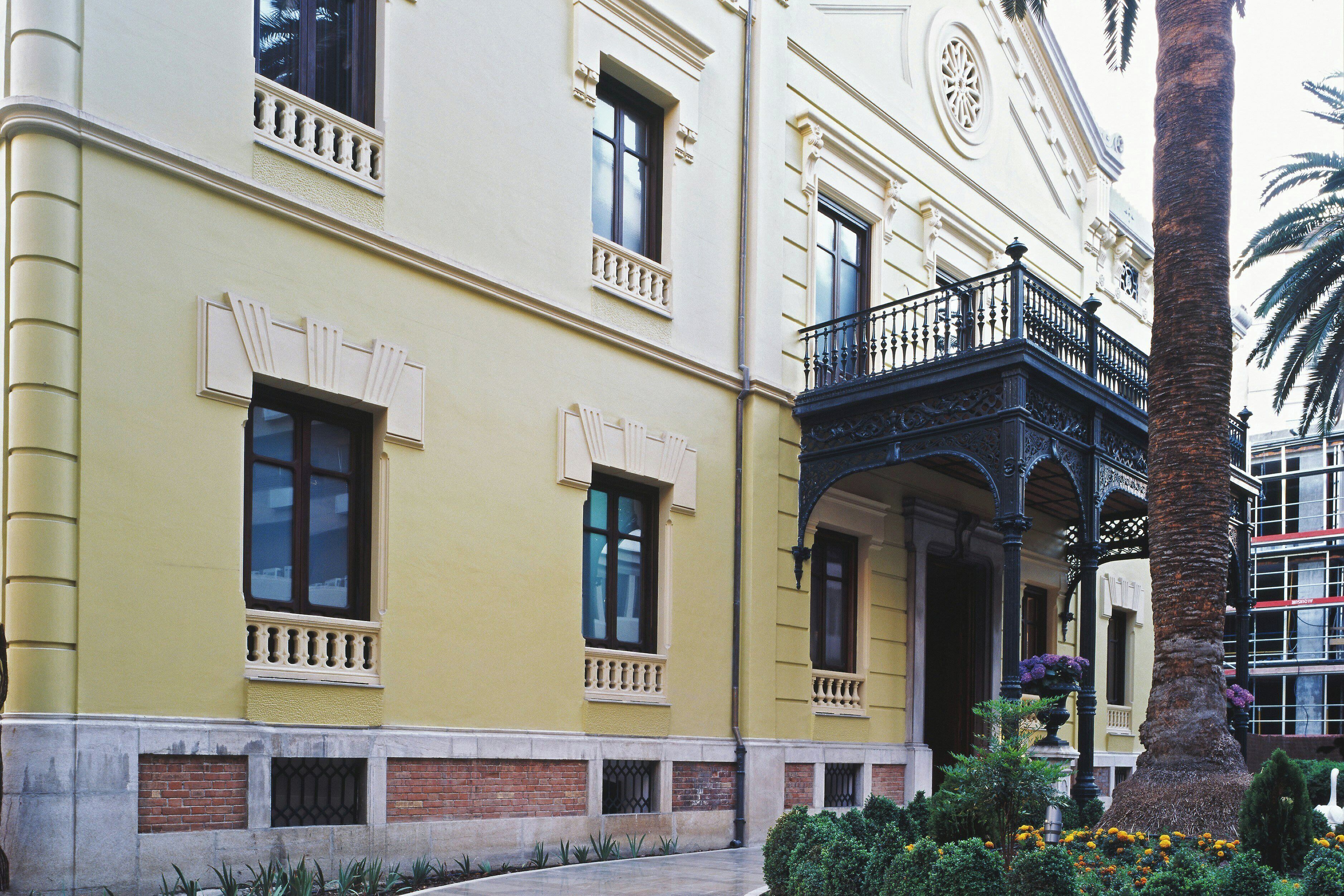 A building with a yellow facade, multiple windows, and a balcony with ornate railings.