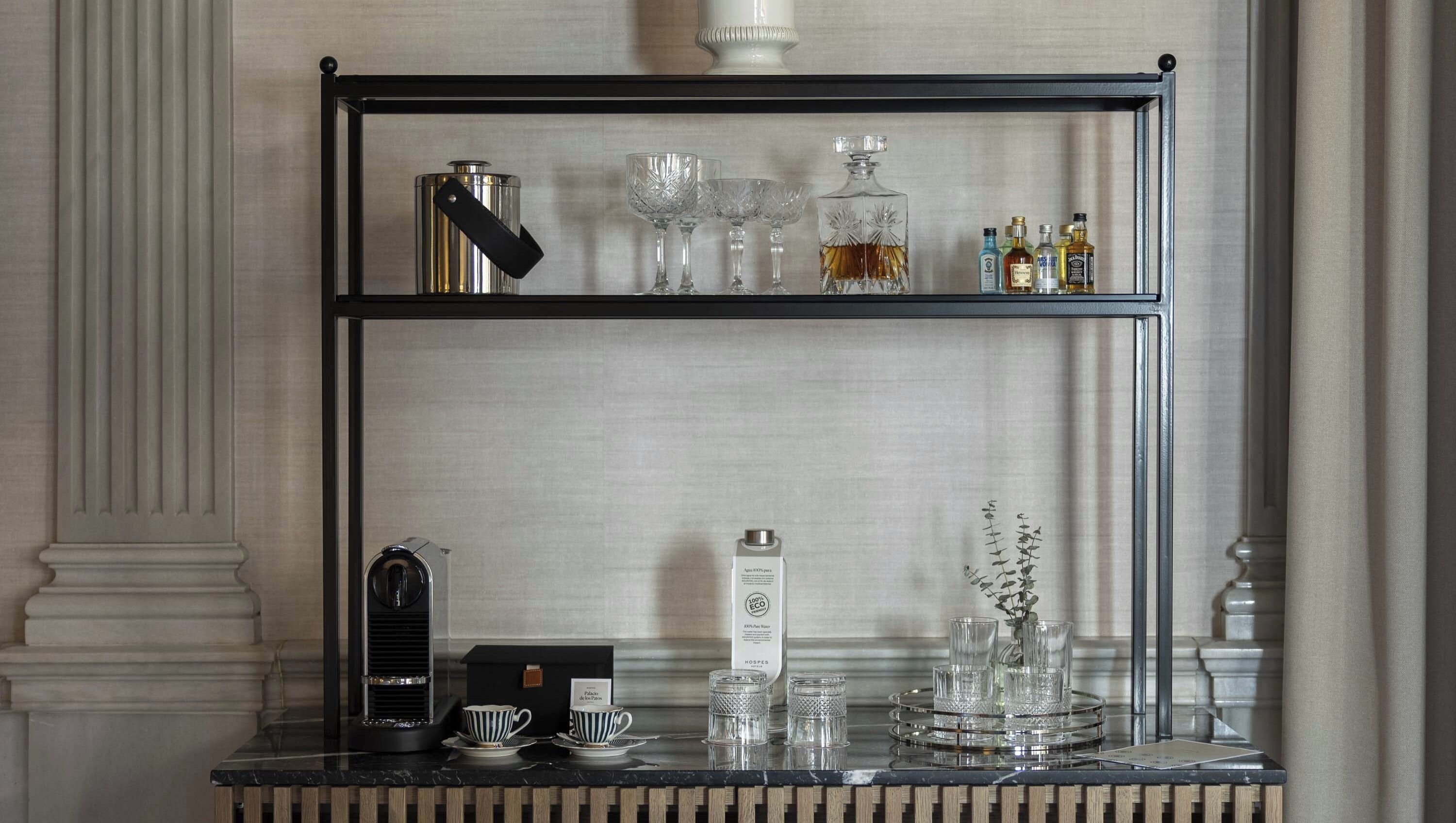 A bar area with a coffee machine, glasses, bottles, and a tray with cups and a vase.