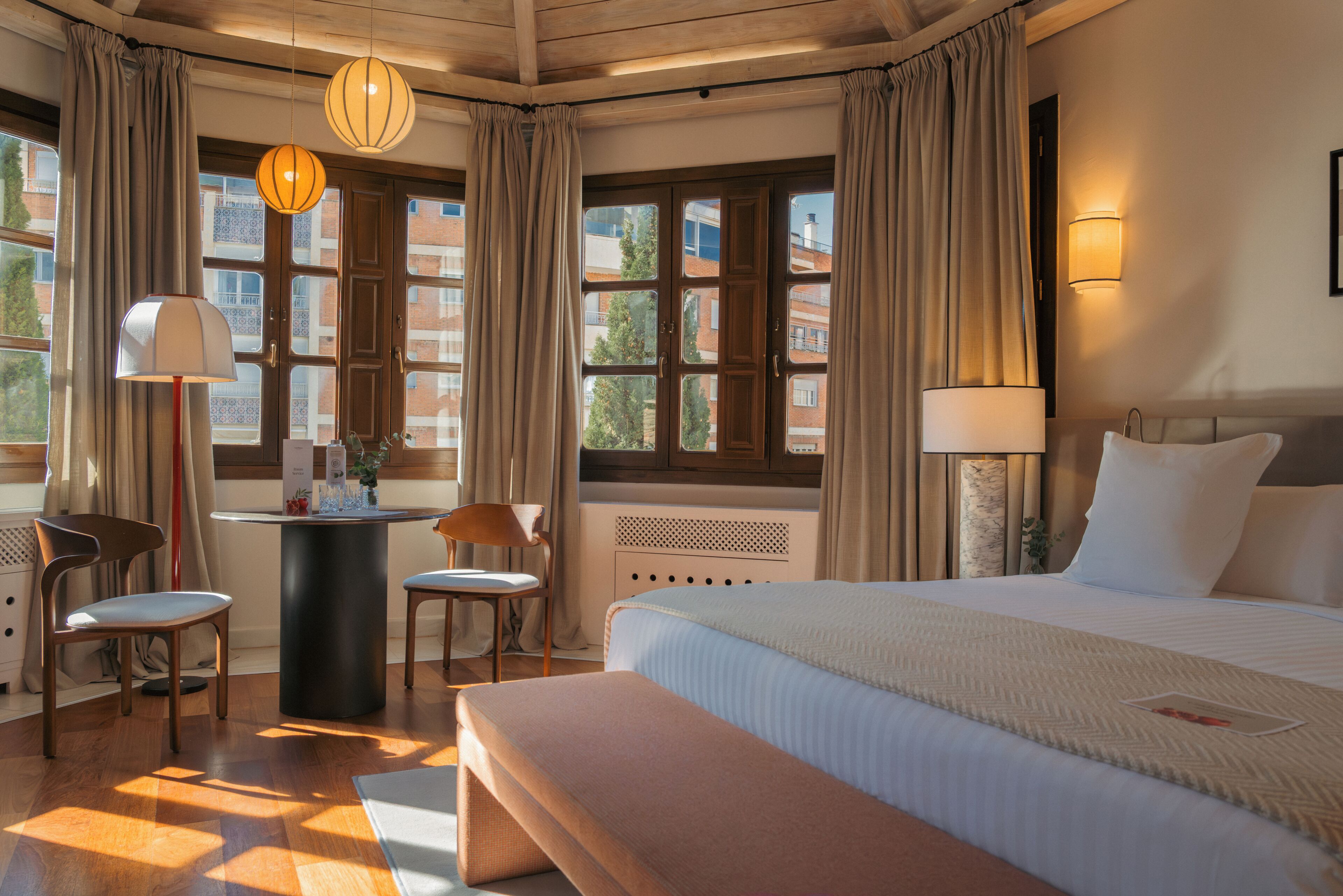 A hotel room with a bed, a desk, two chairs, a table, and a window with curtains.