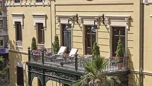 Un bâtiment jaune doté d’un balcon, une fontaine avec des cygnes et un jardin bien entretenu.