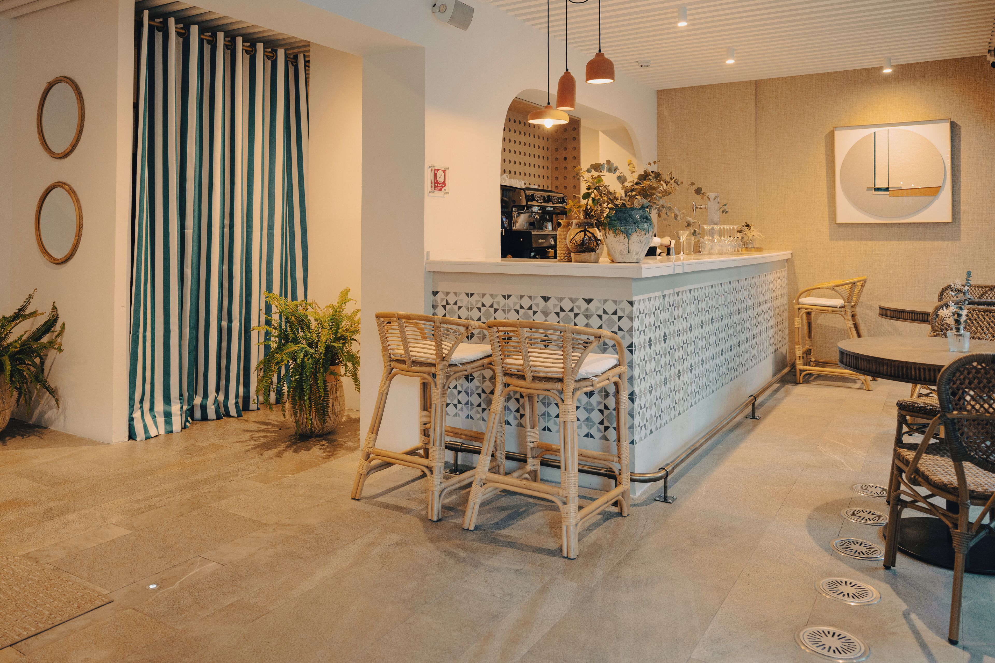 Un interior moderno con una zona de bar, sillas de mimbre y un suelo estampado.