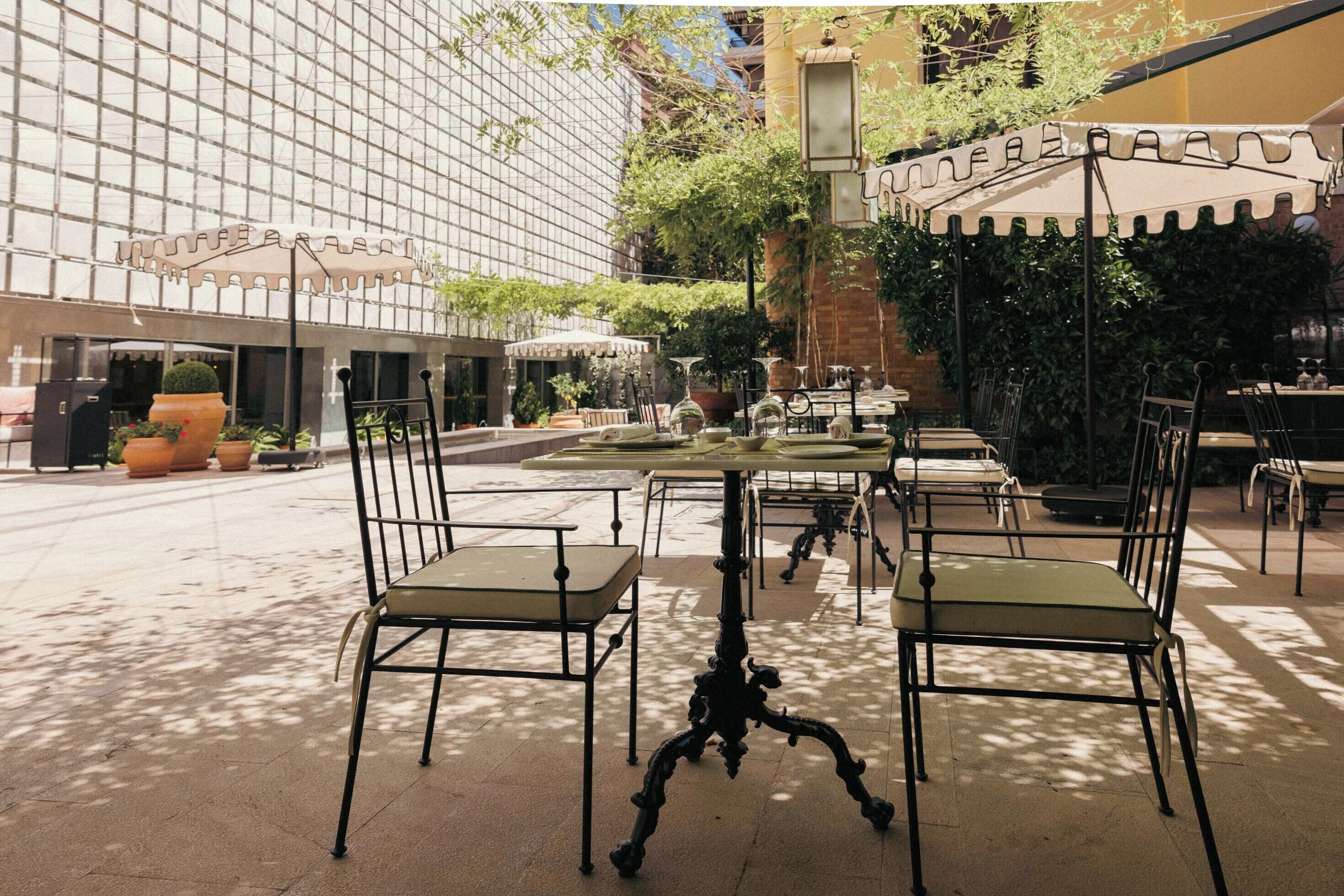 Outdoor seating with tables and chairs, a building with a grid-like facade, and potted plants.