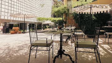 Outdoor seating with tables and chairs, a building with a grid-like facade, and potted plants.