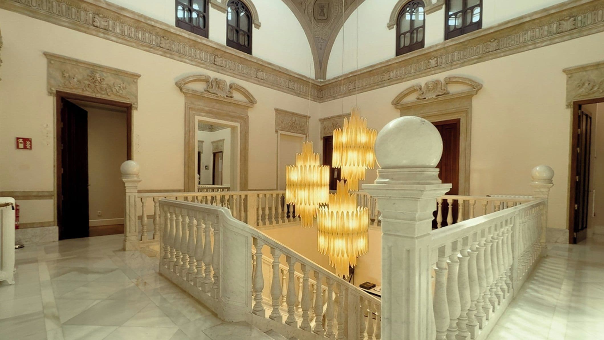 A grand interior with a marble staircase, ornate chandeliers, and classical architectural details.