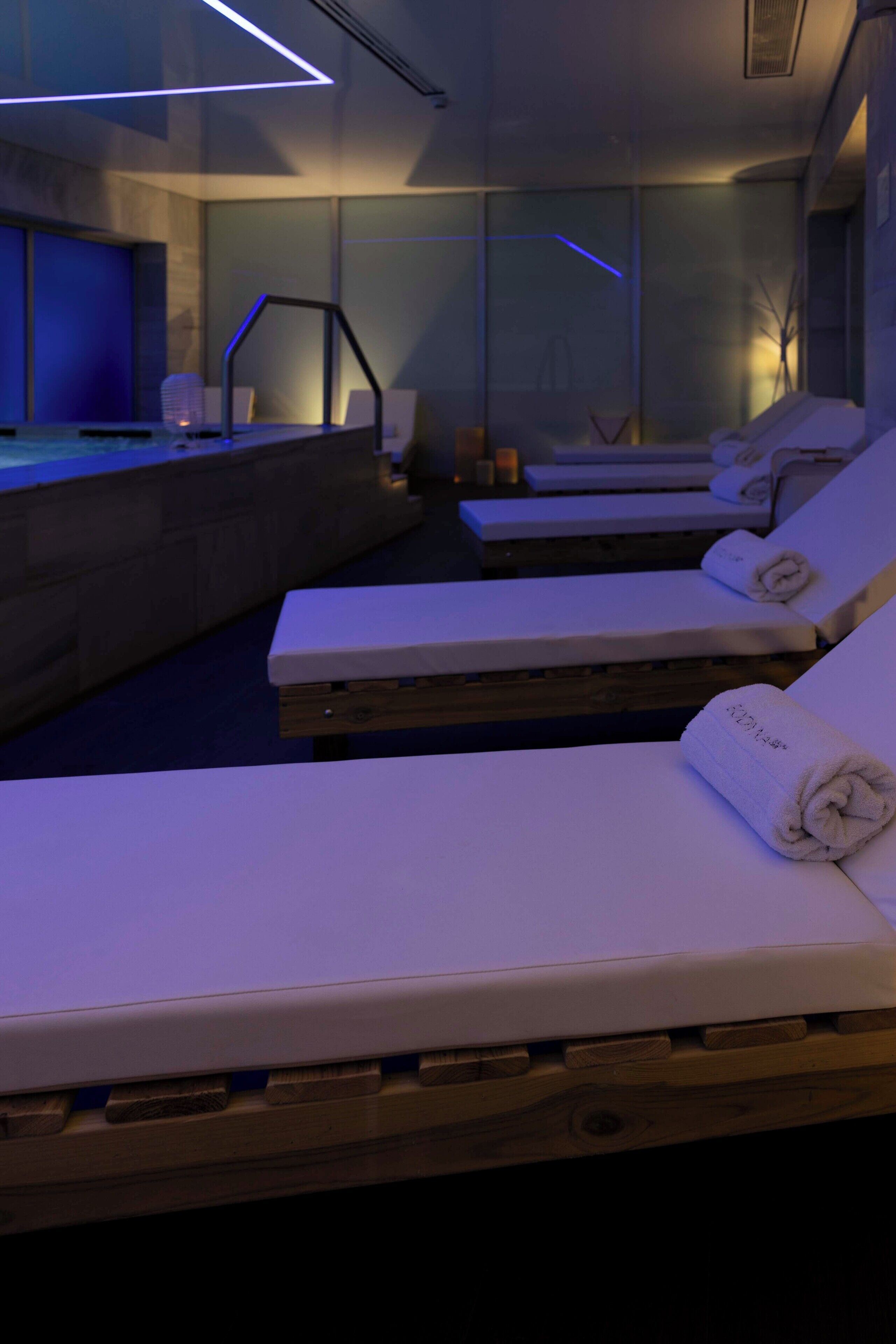 Ett spaområde med solstolar i trä, ett massagebord och en vägg av sten.