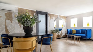 Une pièce moderne avec une table ronde, des chaises bleues et jaunes, un canapé bleu et une plante en pot.