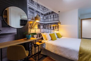 A hotel room with a bed, a desk with a chair, a large mirror, and a wall with a balcony design. - Hotel Presidente (Granada)