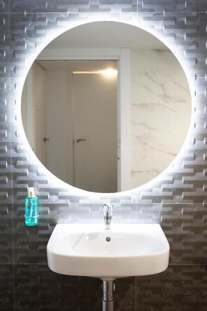 A bathroom with a round mirror, a white sink, and a hand sanitizer dispenser. - Hotel Presidente (Granada)