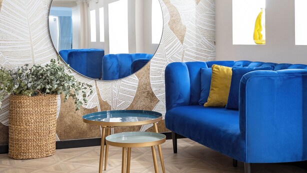 Un salon avec un canapé bleu, un miroir rond, une petite table et une plante en pot.