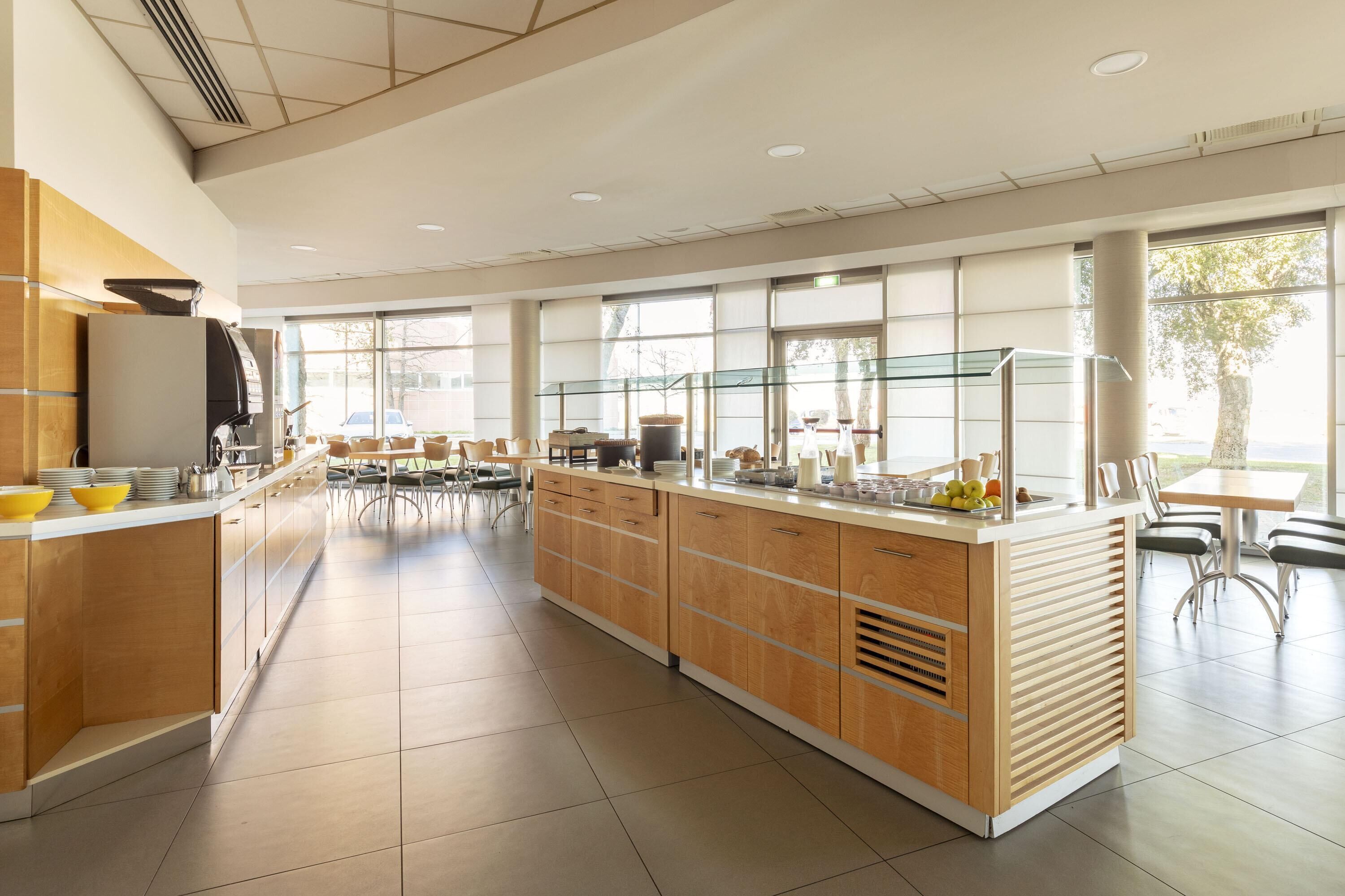 Una amplia cocina con una isla central, ventanas grandes y un comedor con sillas y mesas.