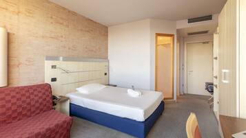 Une chambre d’hôtel avec un lit, un canapé rouge à carreaux, un bureau et un miroir.