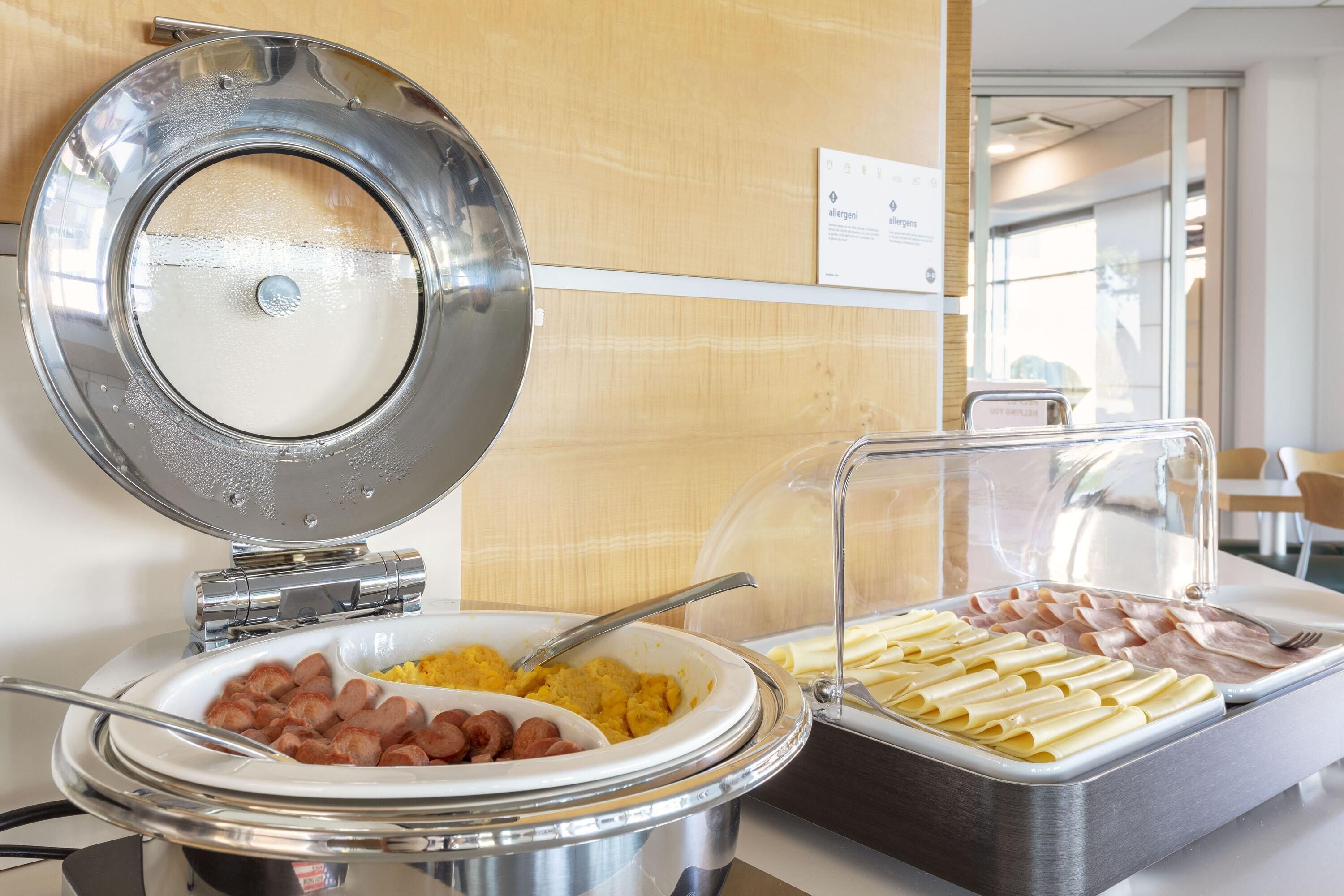 A buffet with various food options including sausages, pasta, and scrambled eggs.