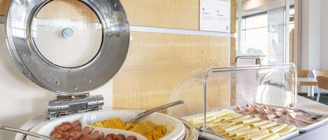 A buffet with various food options including sausages, pasta, and scrambled eggs.